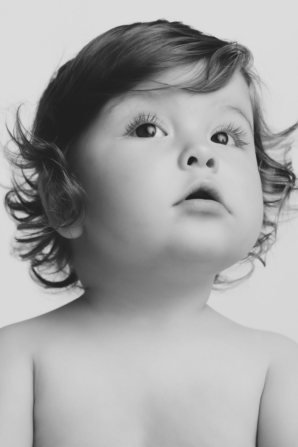 Black and white portrait of an adorable baby with curly hair and big eyes looking up.
