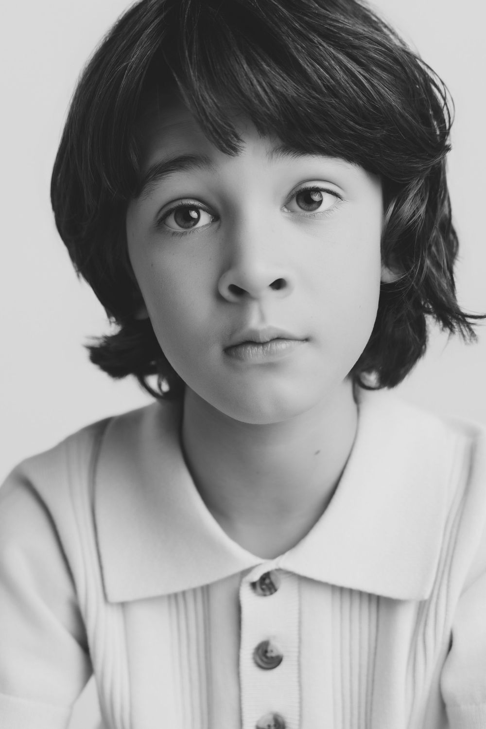 Black and white portrait of a young child with dark hair wearing a collared button-up shirt, looking at camera.