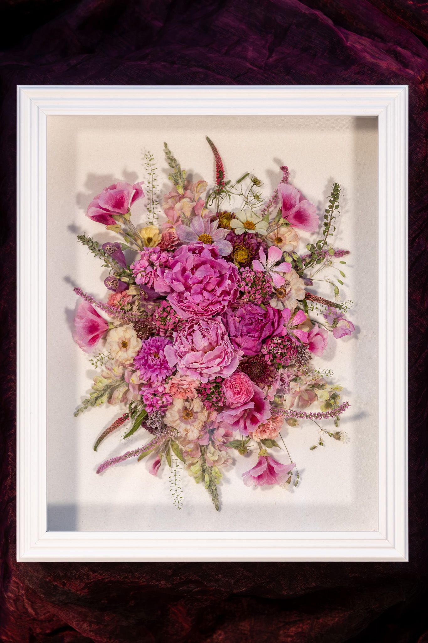 Colorful pressed dried flowers arranged in a rustic wooden frame on white background.