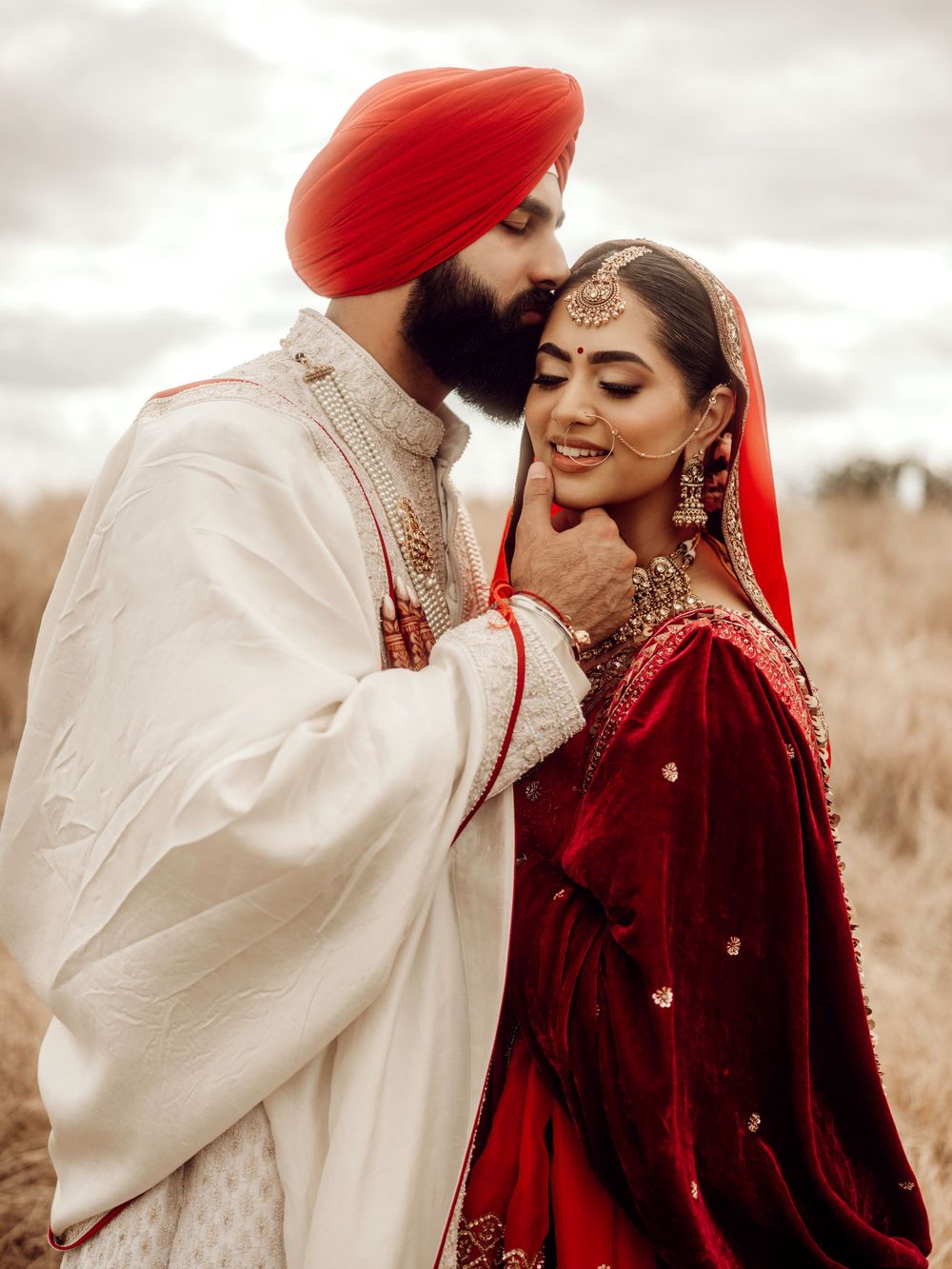 A traditional Sikh wedding couple in formal attire sharing a tender moment against a moody outdoor backdrop.