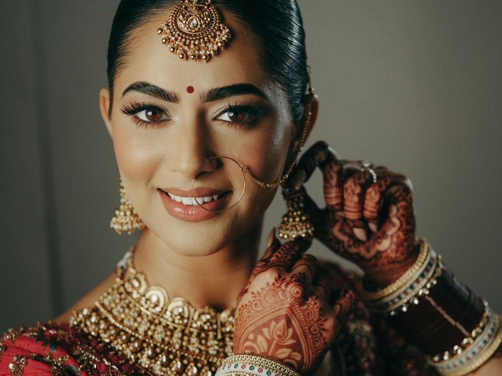 Indian bride wearing traditional gold jewelry and showing intricate henna designs on her hands while smiling joyfully.