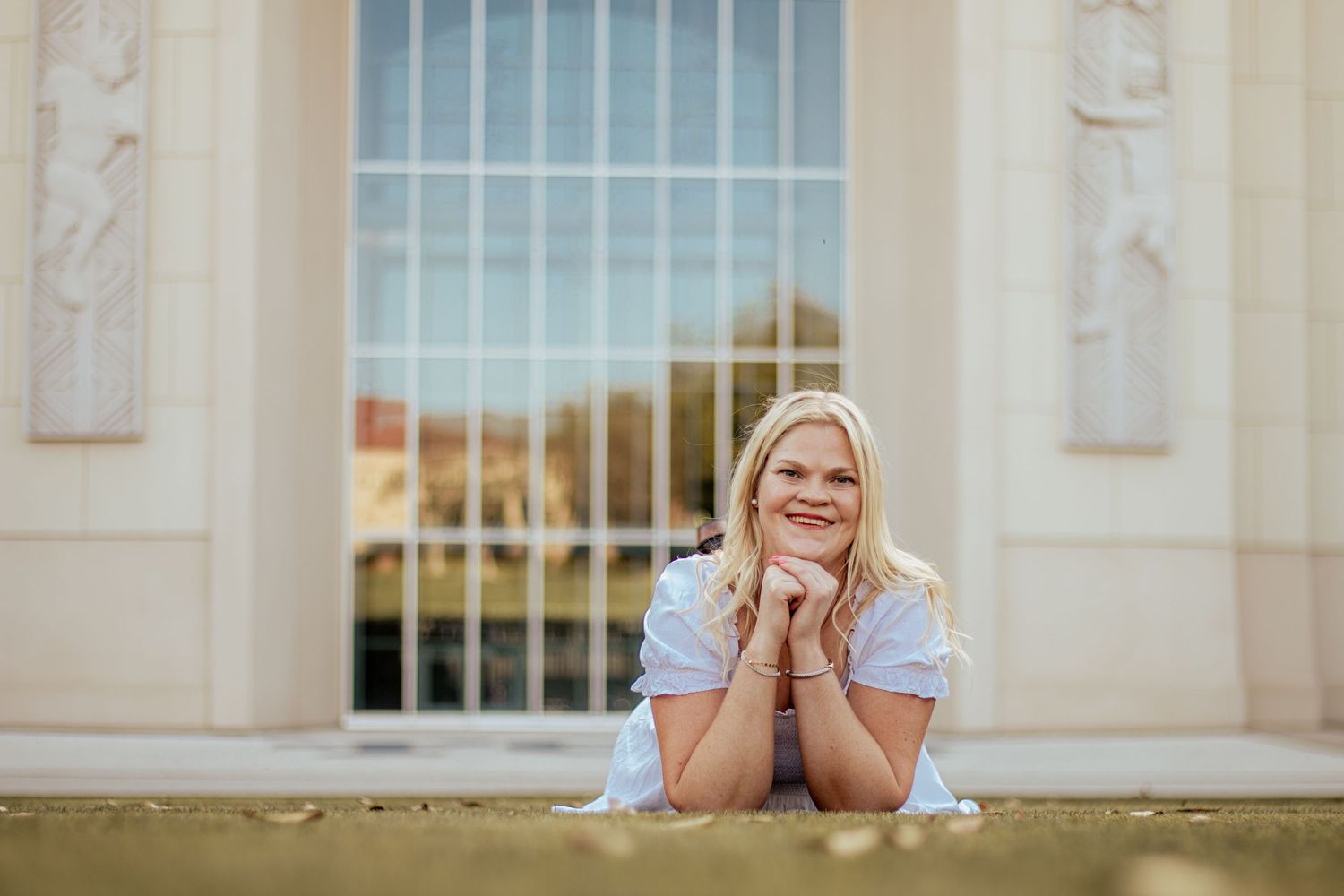 A student sits smiling on stone steps outside a classical building with columns and arched windows.