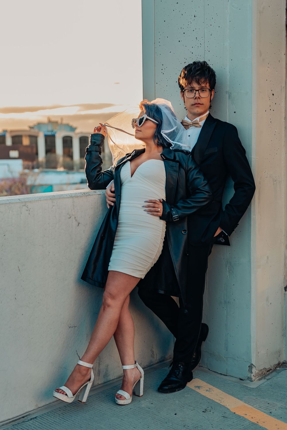 Artistic wedding photoshoot featuring couple posing against industrial setting.