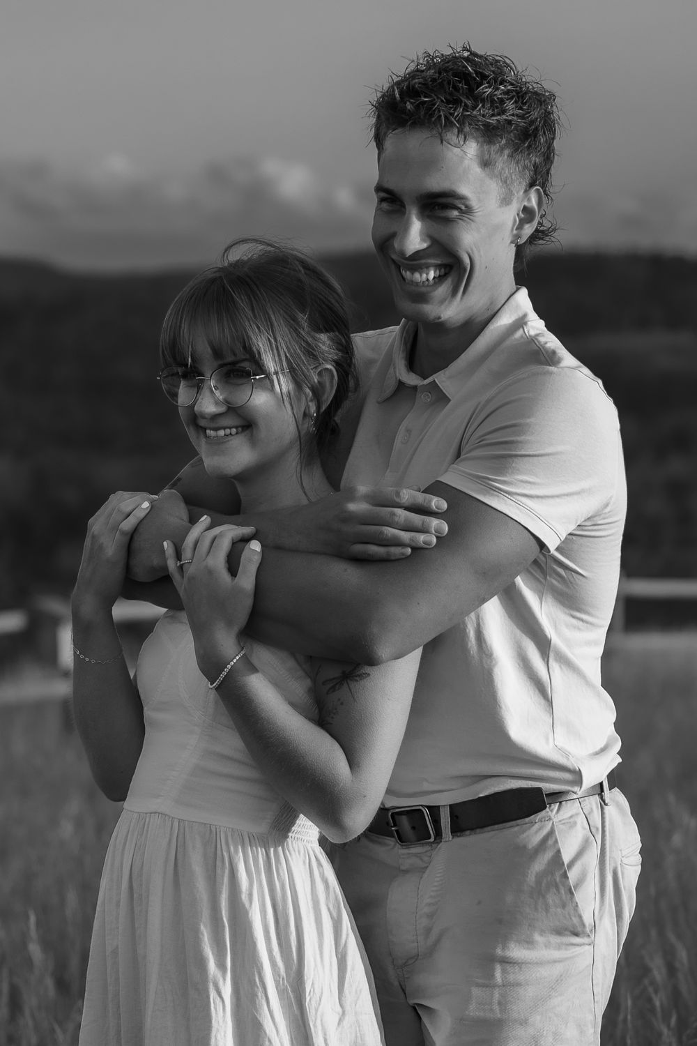 Black and white portrait of couple embracing in field with joyful expressions.