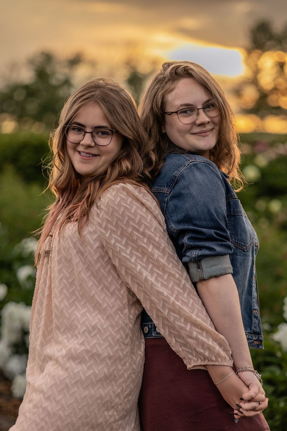 Two friends posing back-to-back in a garden during golden hour.