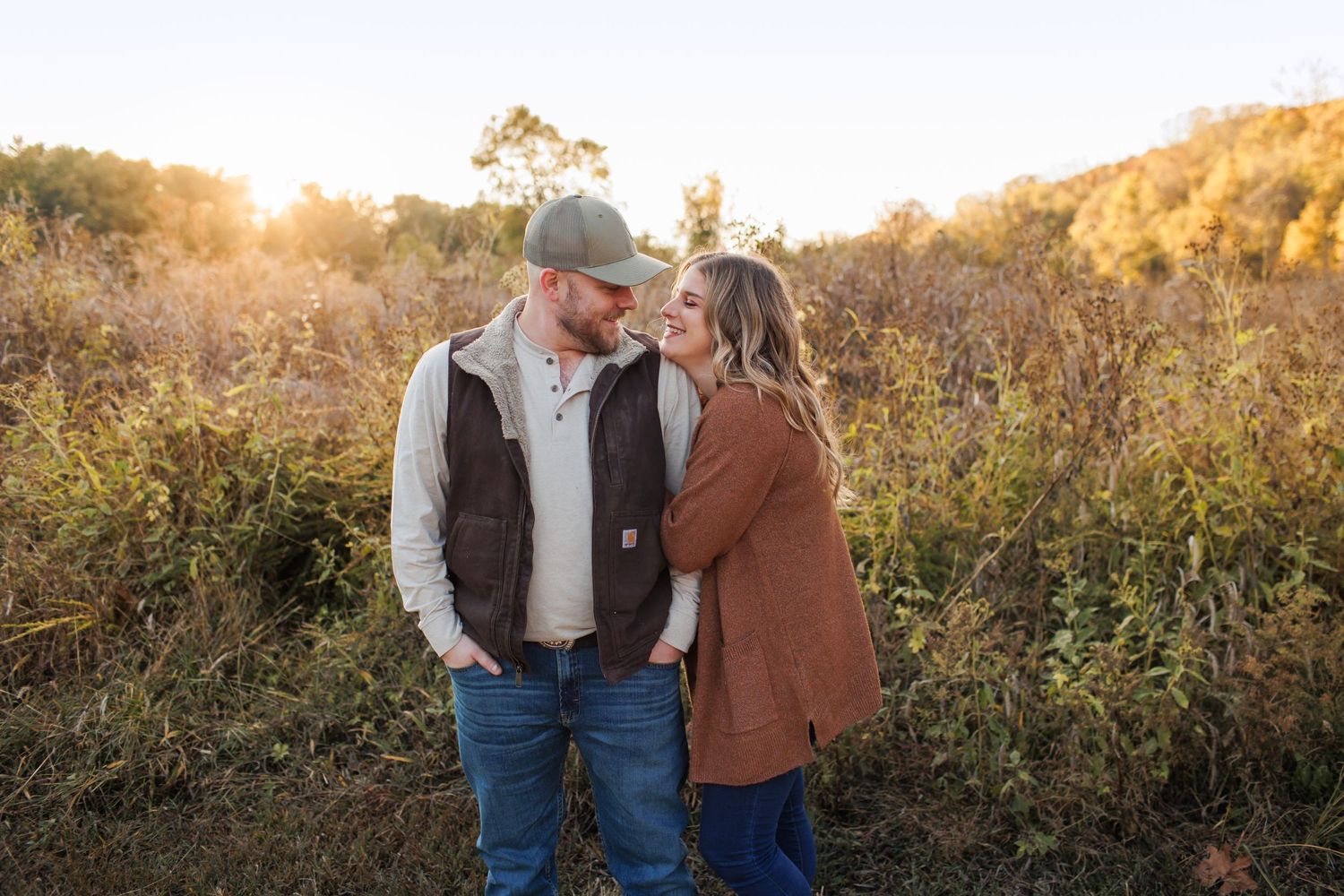 Couple sharing intimate moment during golden hour in fall field with sunset glow.