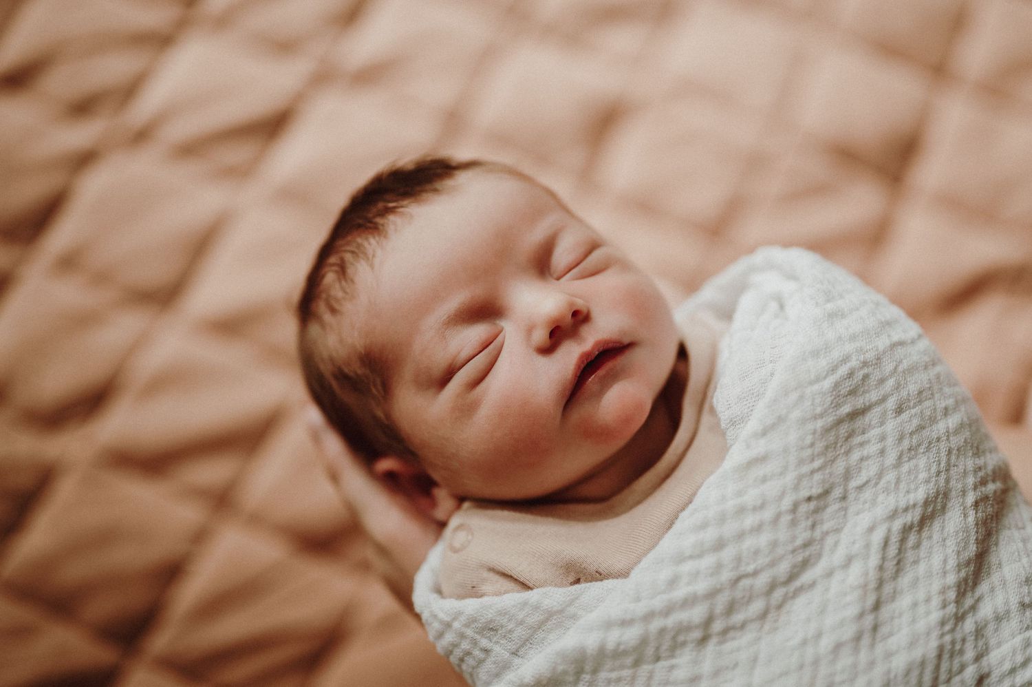 Closeup portrait of a sleeping baby wrapped in white swaddling.