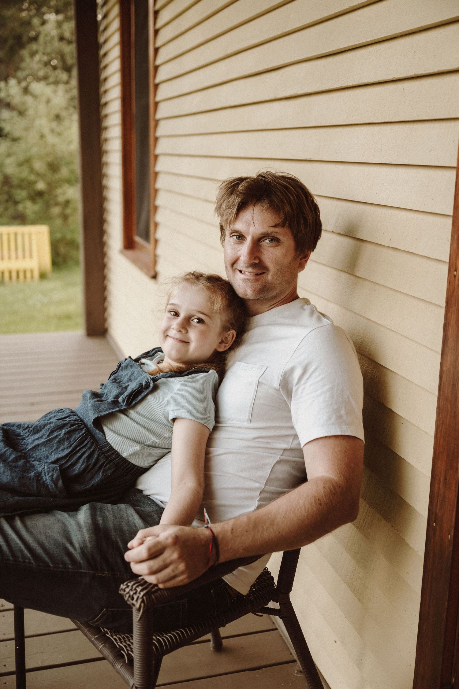A parent and child relaxing together on a porch chair.