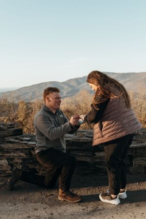 A proposal moment captured at a scenic mountain overlook with mountains in the background during sunset.