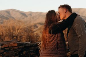 A romantic moment shared between two people on a mountain overlook at sunset.