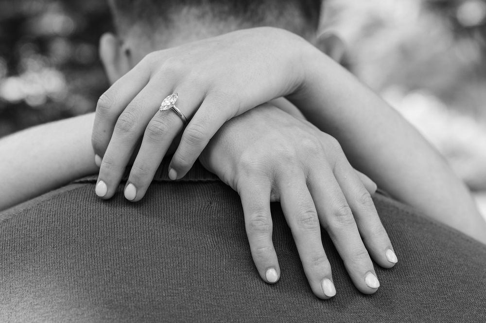Black and white photo of a couple embracing, showcasing an elegant diamond engagement ring on the woman's hand.