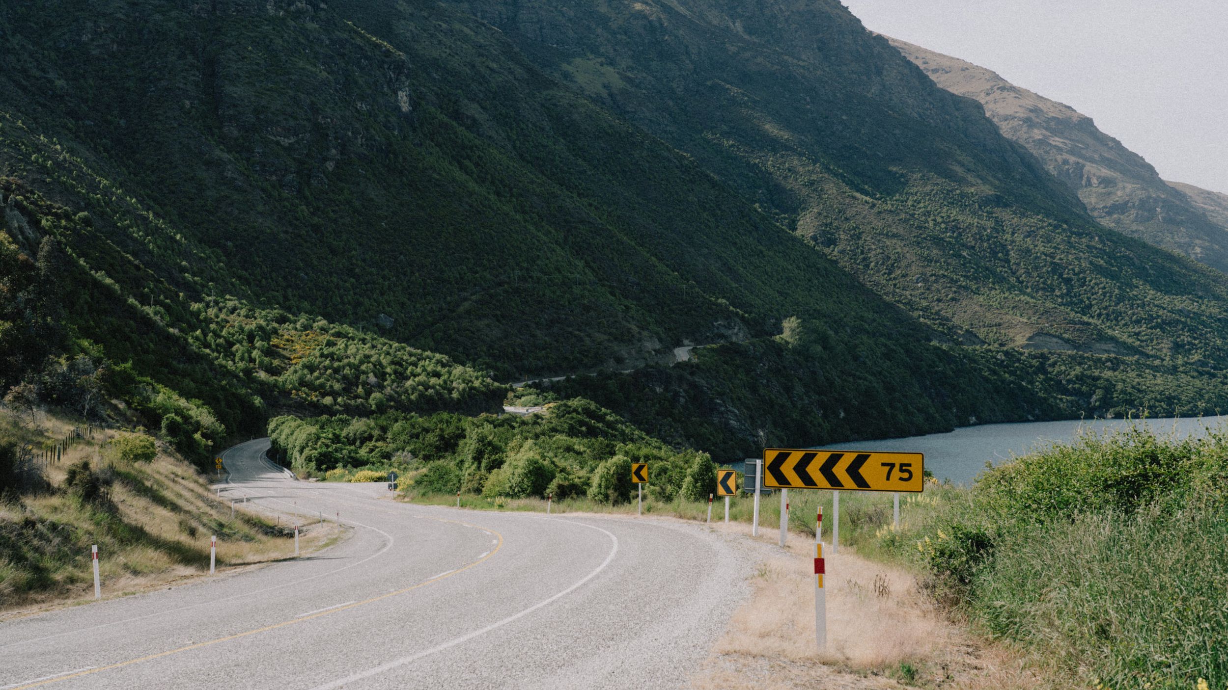 A winding mountain road with yellow arrow warning signs against a backdrop of green hills.