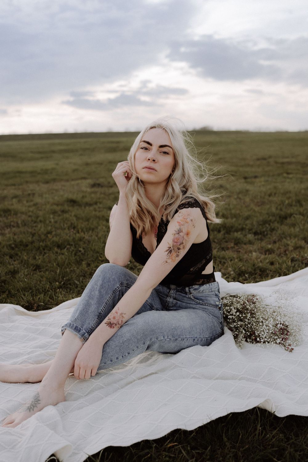 Casual outdoor portrait on blanket in field at sunset with visible tattoos.