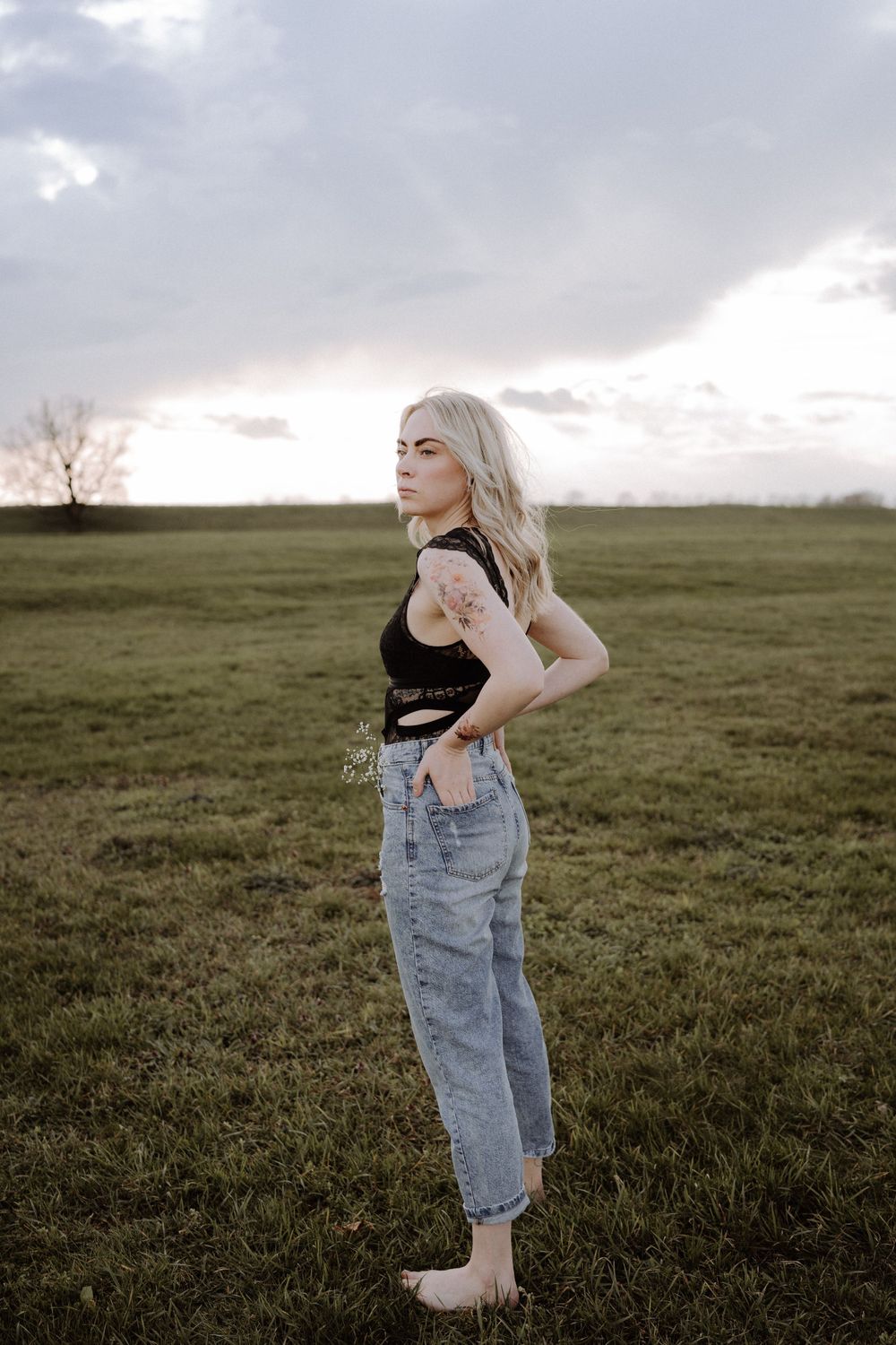 Woman in casual attire poses in open field during golden hour.
