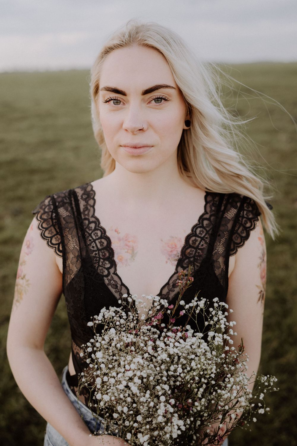 Portrait in black lace dress holding baby's breath bouquet in grassy field.