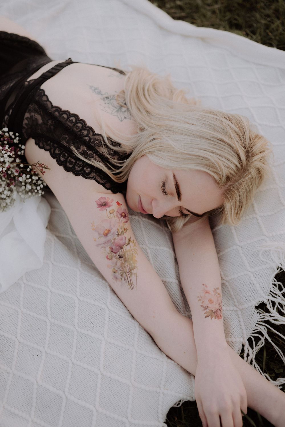 Artistic portrait lying on white blanket with floral tattoos and black lace.