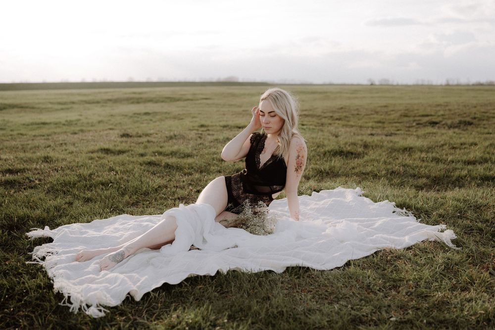 Outdoor portrait session on white blanket in vast green field.