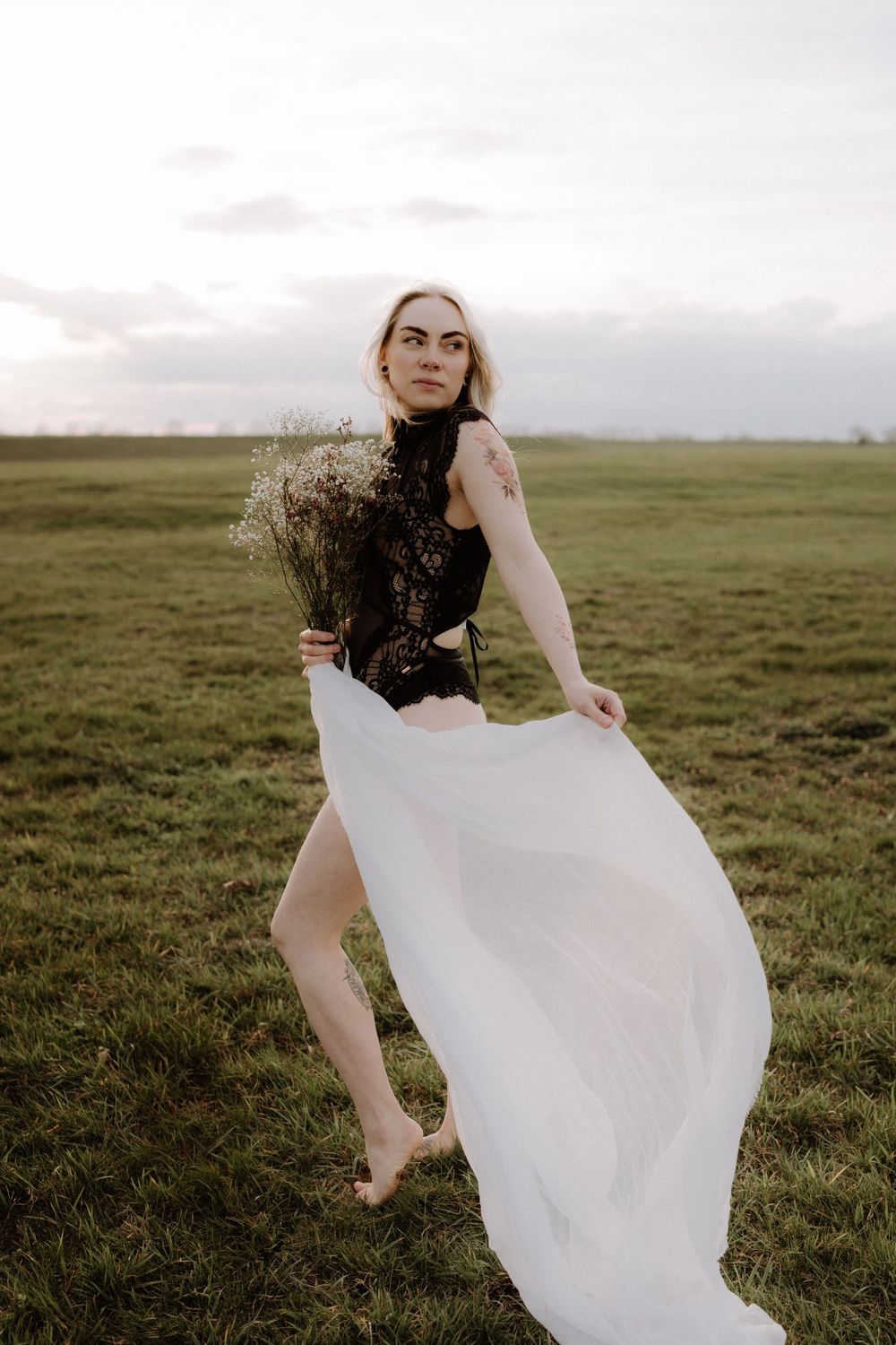 Ethereal portrait in a field with black lace top and flowing white skirt holding dried flowers at sunset.