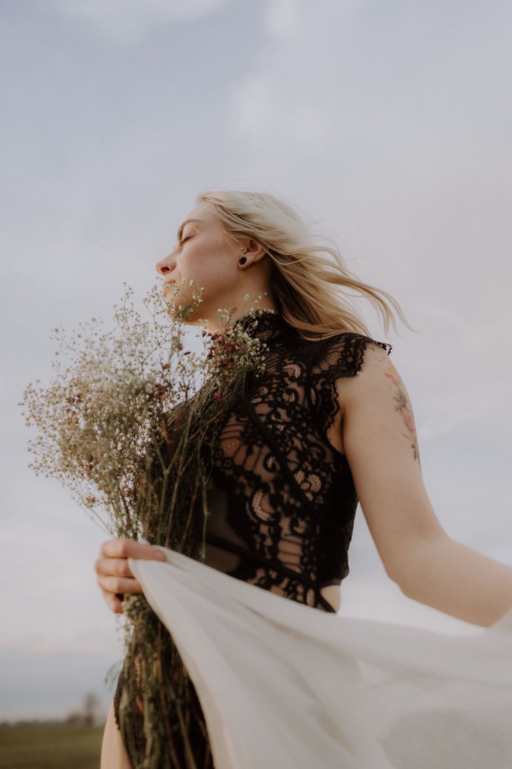 Artistic portrait with windswept hair holding dried flowers in black lace and white fabric.