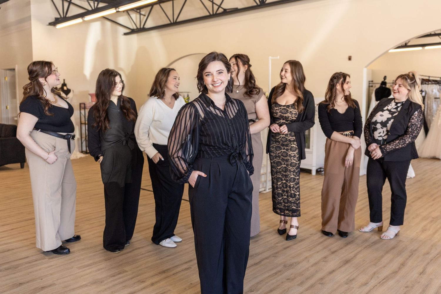 A group of women in elegant attire gather in a bright bridal boutique showroom.