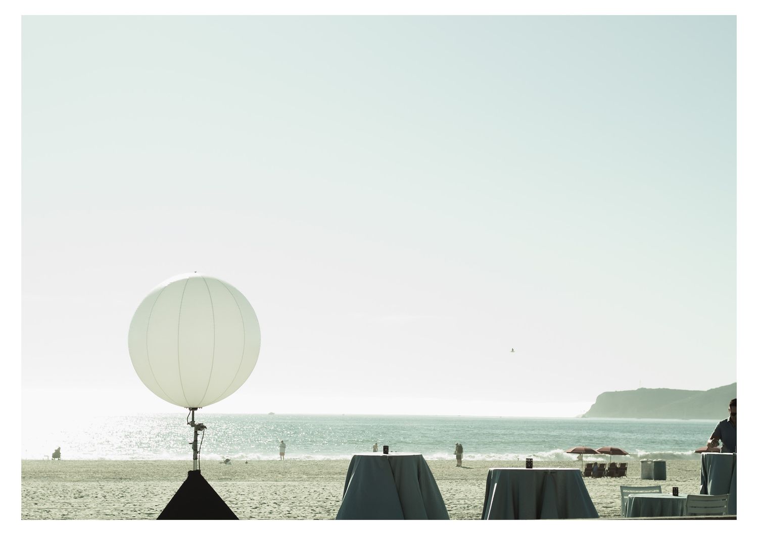 White balloons float against a misty beach horizon creating a dreamy atmosphere.