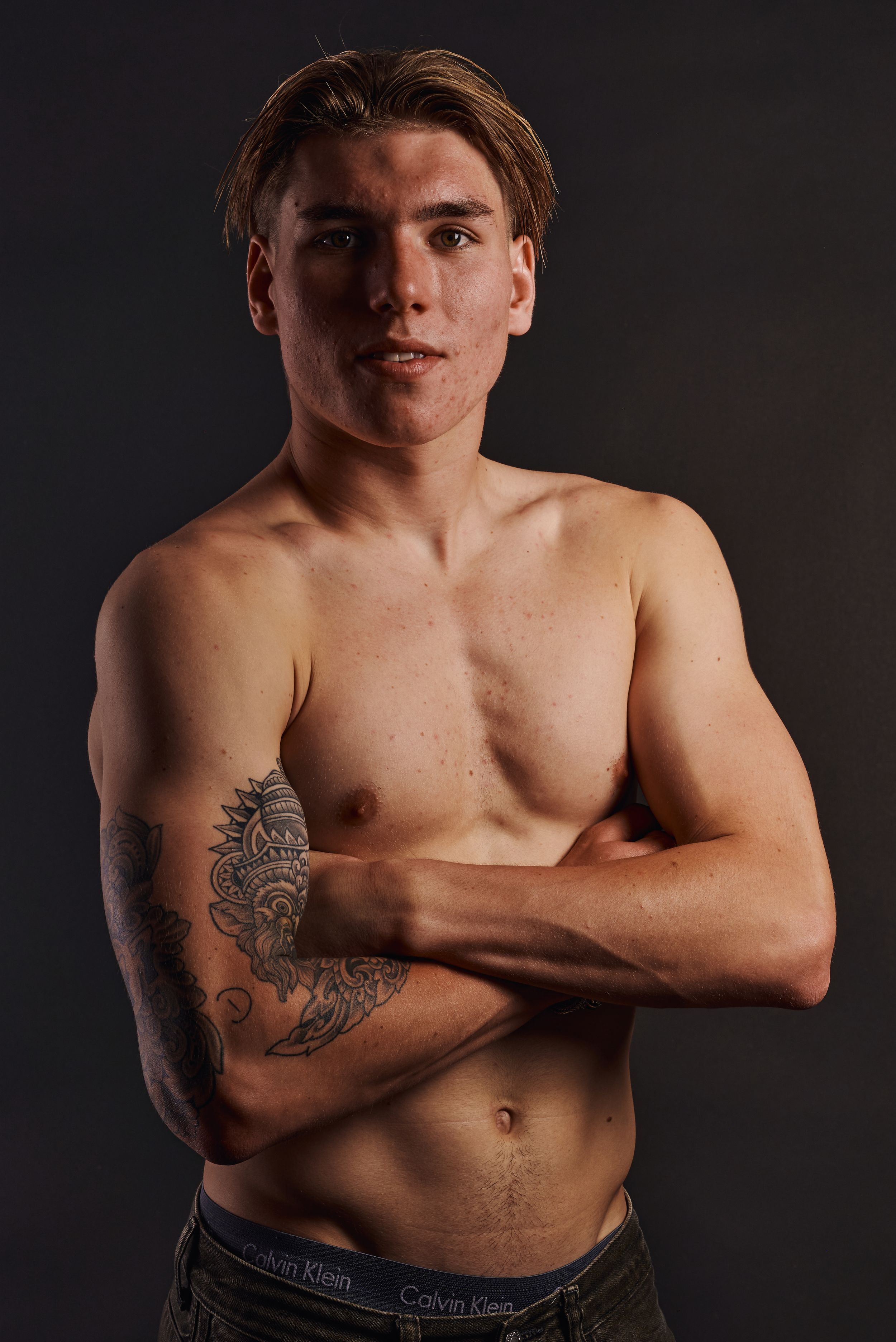 Jonge man zonder shirt met armen gekruist en tattoos en sleeve tattoo