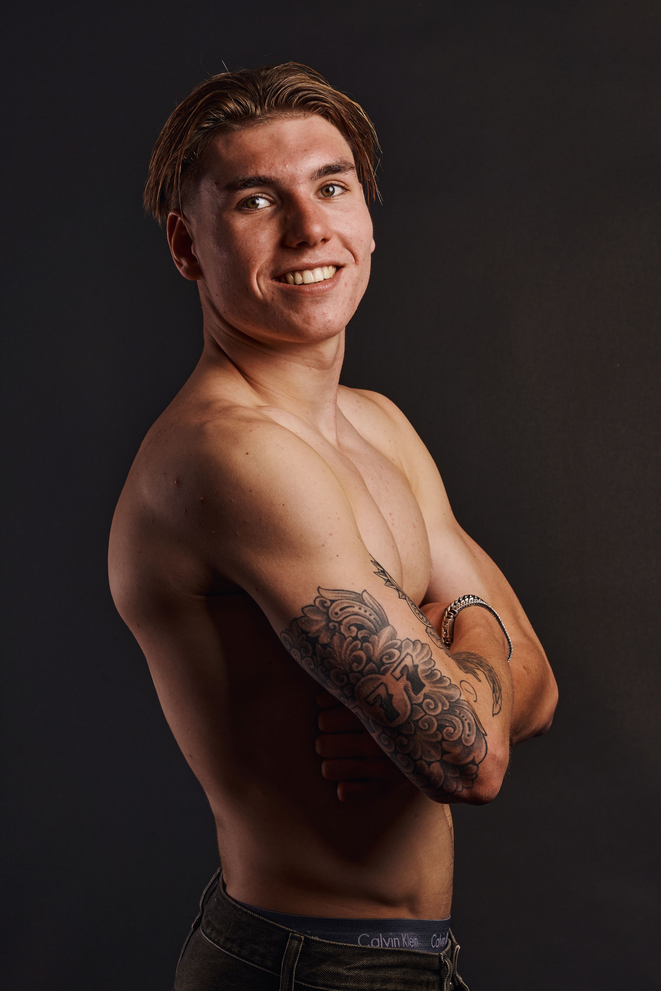 Jonge man zonder shirt met armen gekruist en tattoos en een zelfverzekerde glimlach