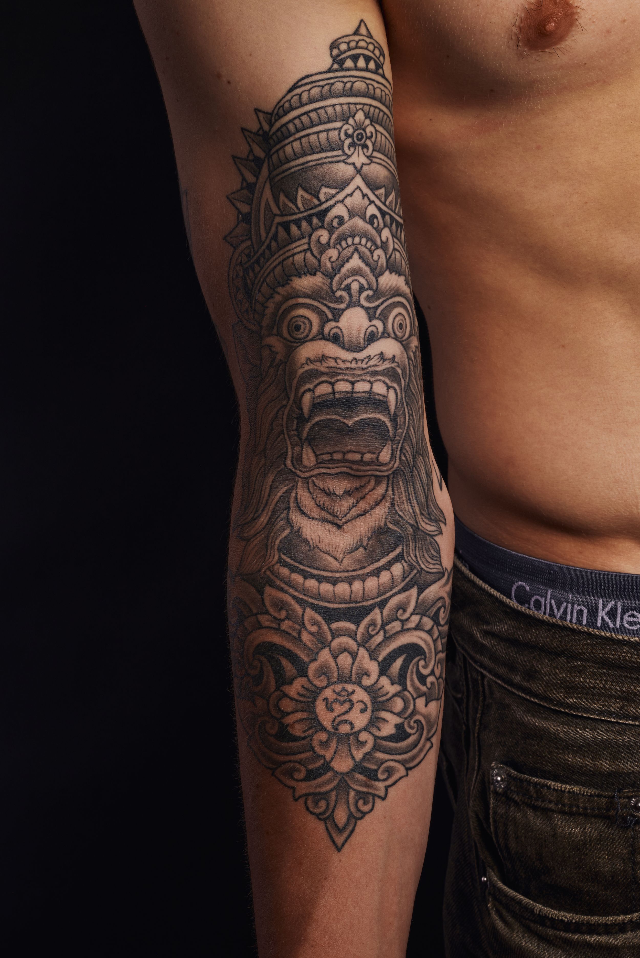Detailed Balinese deity blackwork tattoo sleeve on male forearm.
