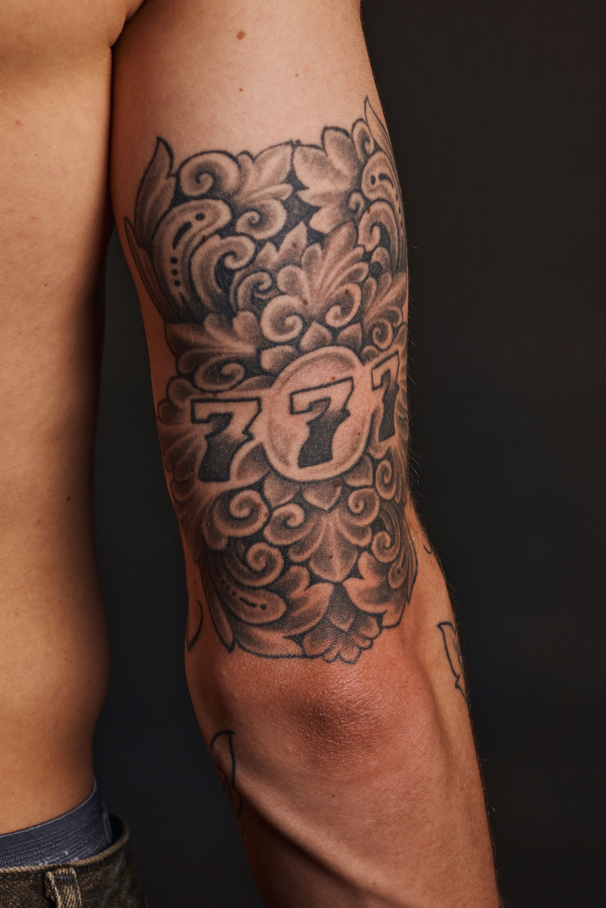 Ornate black and grey lucky 777 elbow tattoo with floral design.