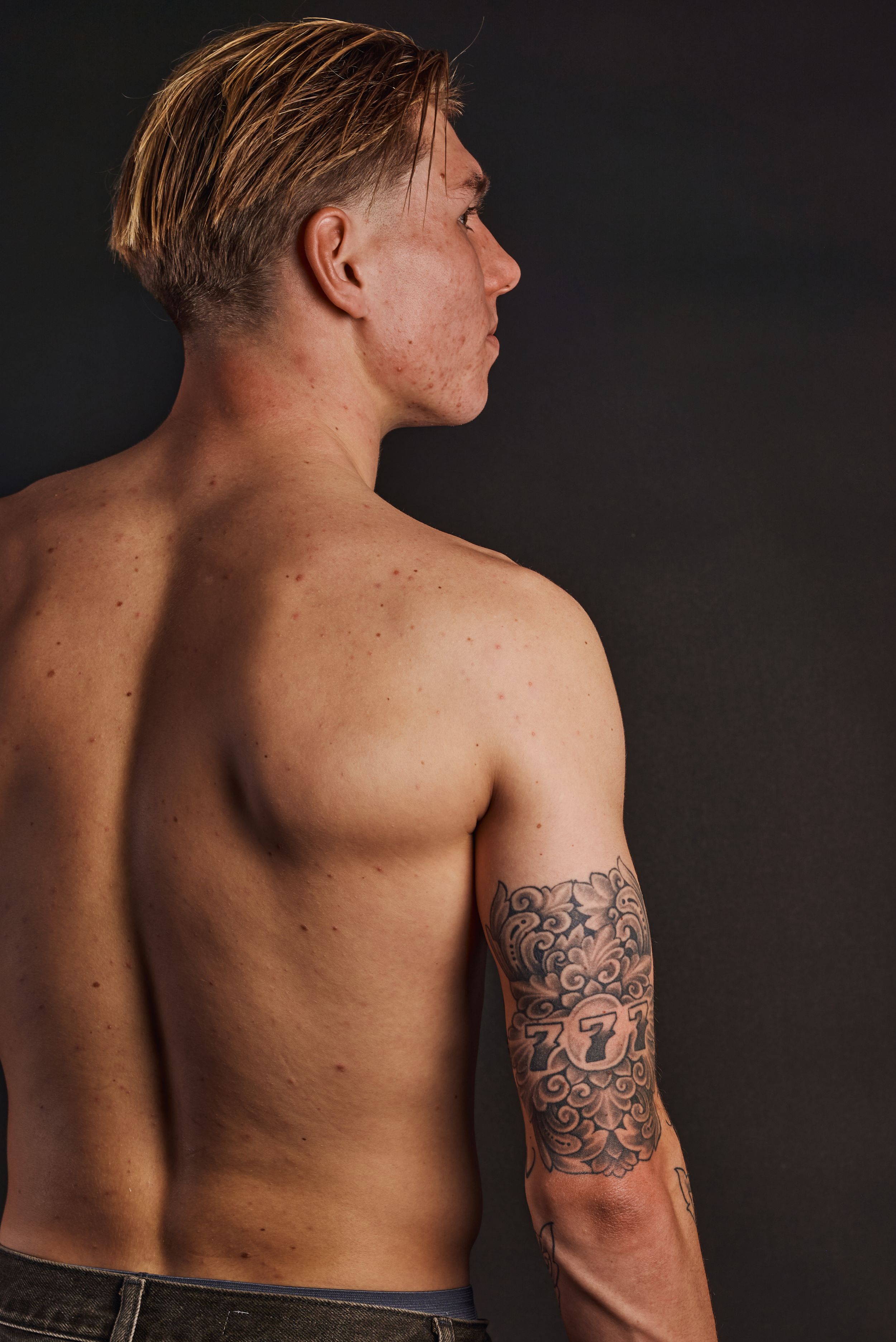 Jonge man zonder shirt van met een tattoo op zijn arm met een 777 motief.