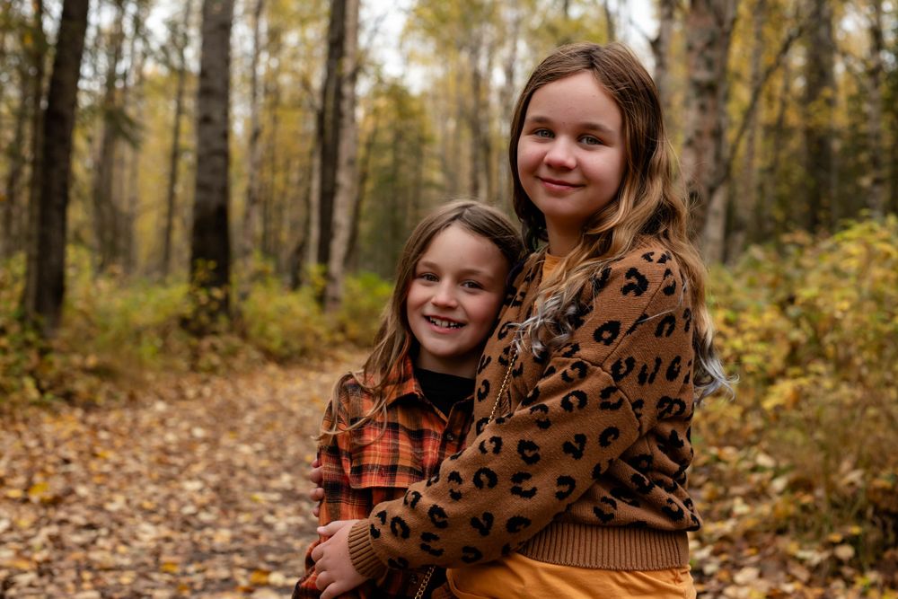 Two young people in autumn wear share a warm embrace on a leaf-covered forest path.