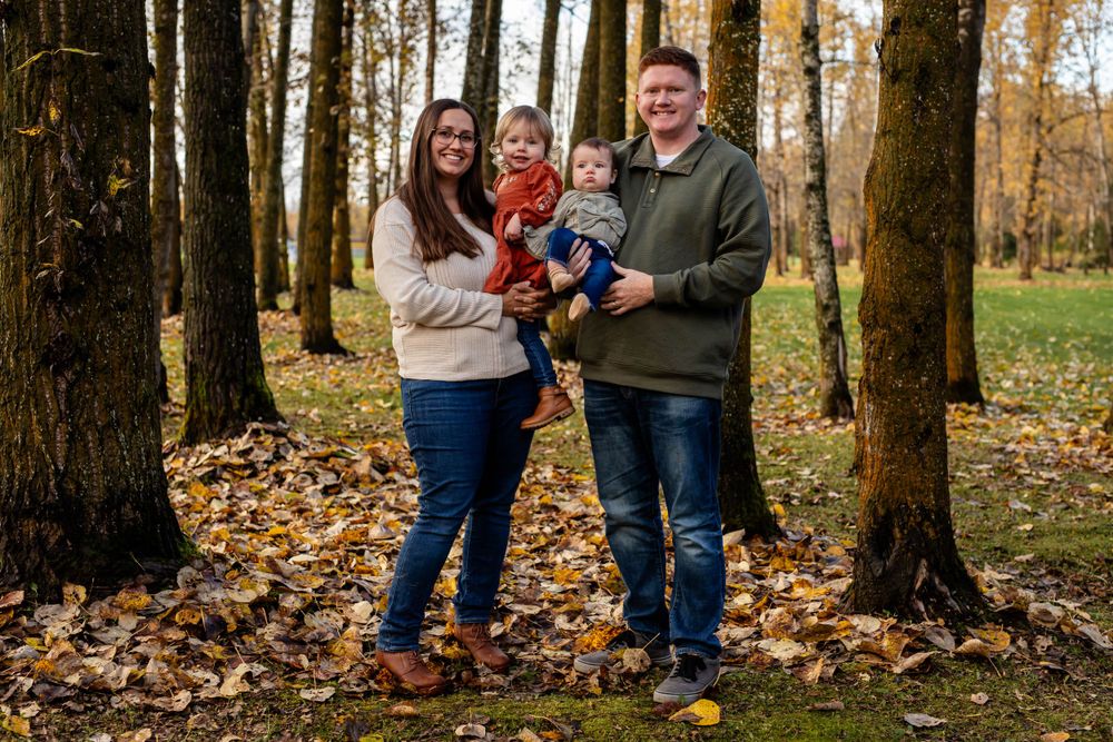 Family portrait captured among fall foliage and trees on autumn day.