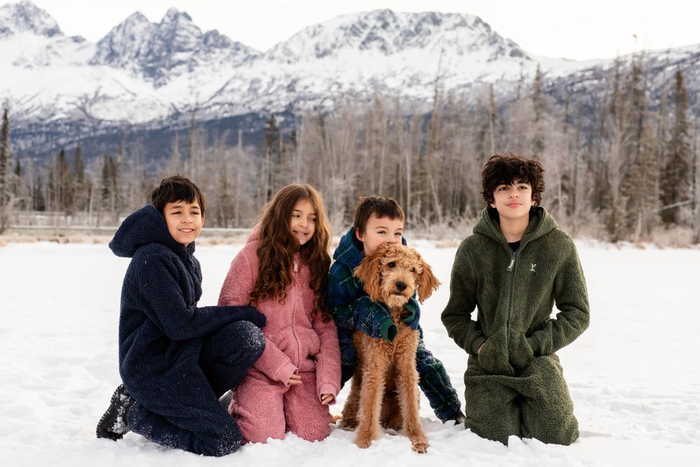 Group posing with their airedale terrier dog in a snowy mountain landscape with snow-capped peaks.
