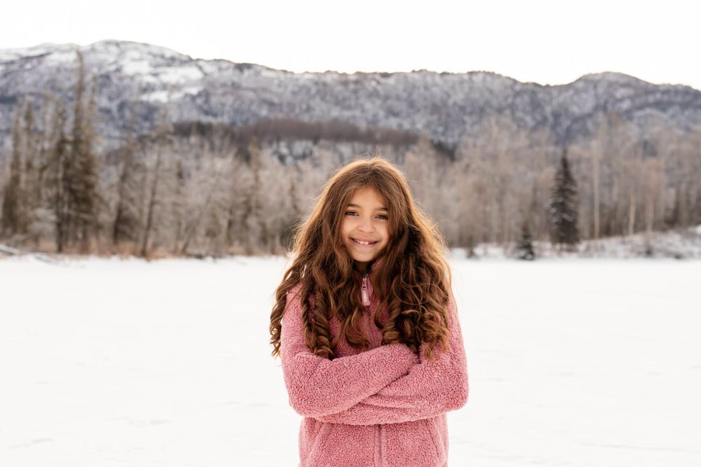 Person in pink sweater poses in snowy landscape with mountain backdrop.