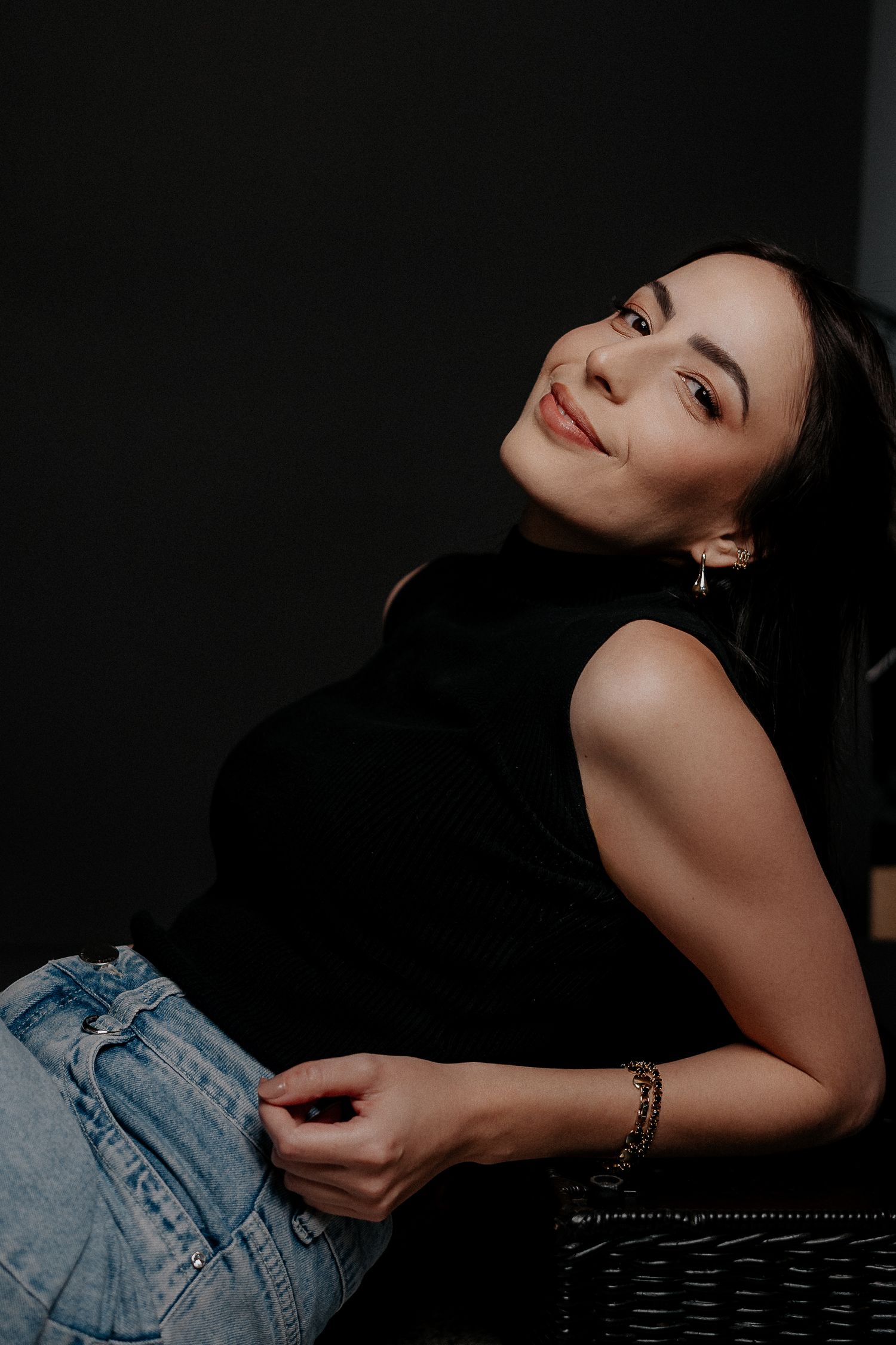 Um retrato sobre fundo preto com jeans casual e blusa preta elegante.
