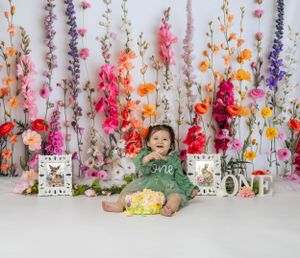 Baby during One Wild Flower-themed cake smash in Chicago IL studio with colorful floral backdrop, greenery, and playful wildflower decor.