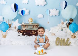 Baby during One Trip Around the Earth-themed cake smash in Glenview IL studio featuring hot air balloons, clouds, and travel-inspired decor.