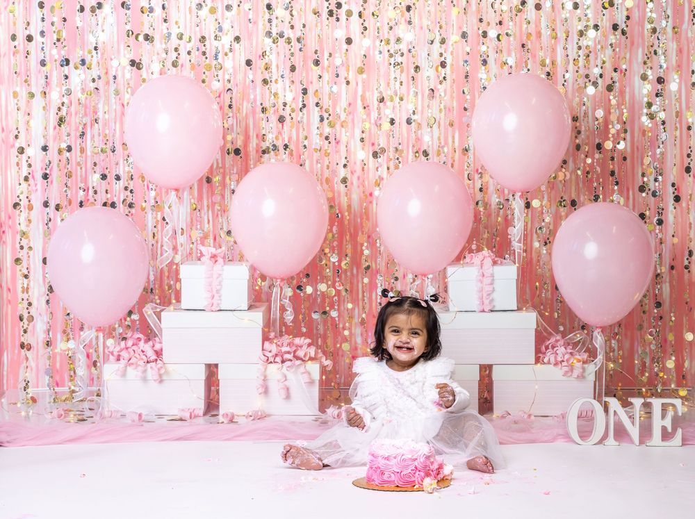 Baby during glam pink-themed cake smash in Glenview IL studio with balloons, confetti backdrop, and matching cake for first birthday.