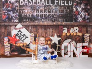 Baby celebrating first birthday with baseball-themed cake smash in Glenview IL studio featuring bats, scoreboard, and fun props.