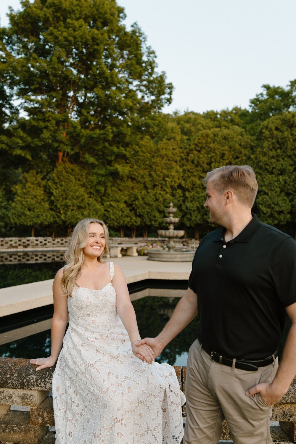 A couple shares a loving moment while sitting on a stone wall surrounded by lush greenery.