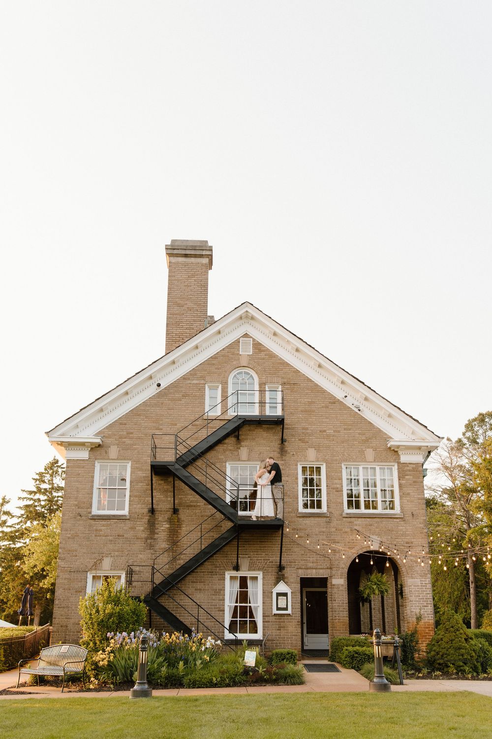 A elegant brick building with white trim and fire escape stairs stands proudly on a manicured lawn.