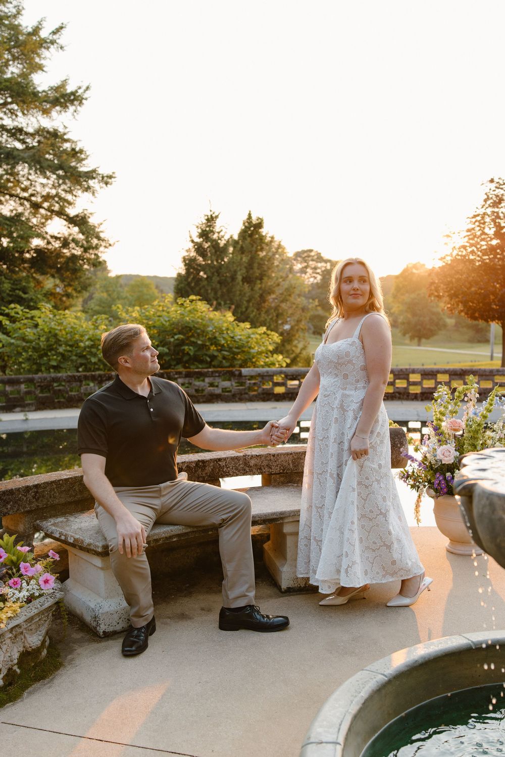 A couple in formal attire poses on stone steps near a reflecting pool during golden hour.