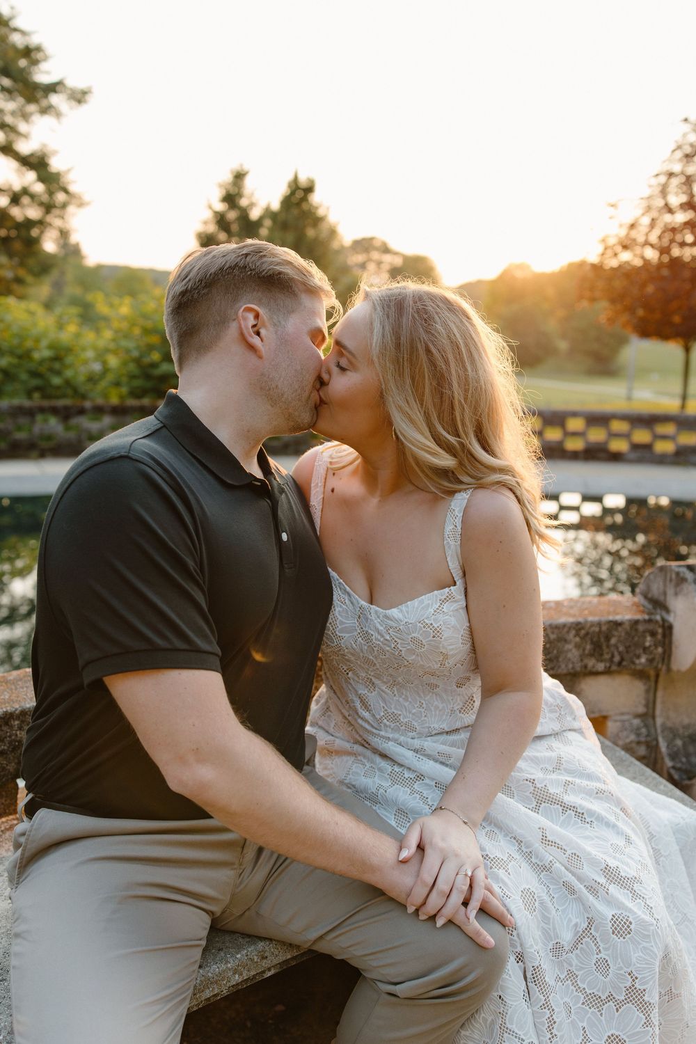 A couple in wedding attire sits together on a stone wall at sunset by a waterfront, captured in multiple romantic poses.