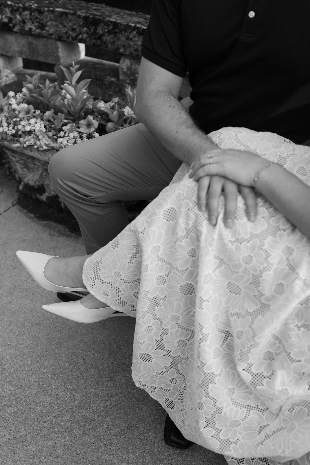 Black and white detail shot of a lace dress and gray slacks while sitting on stone steps.
