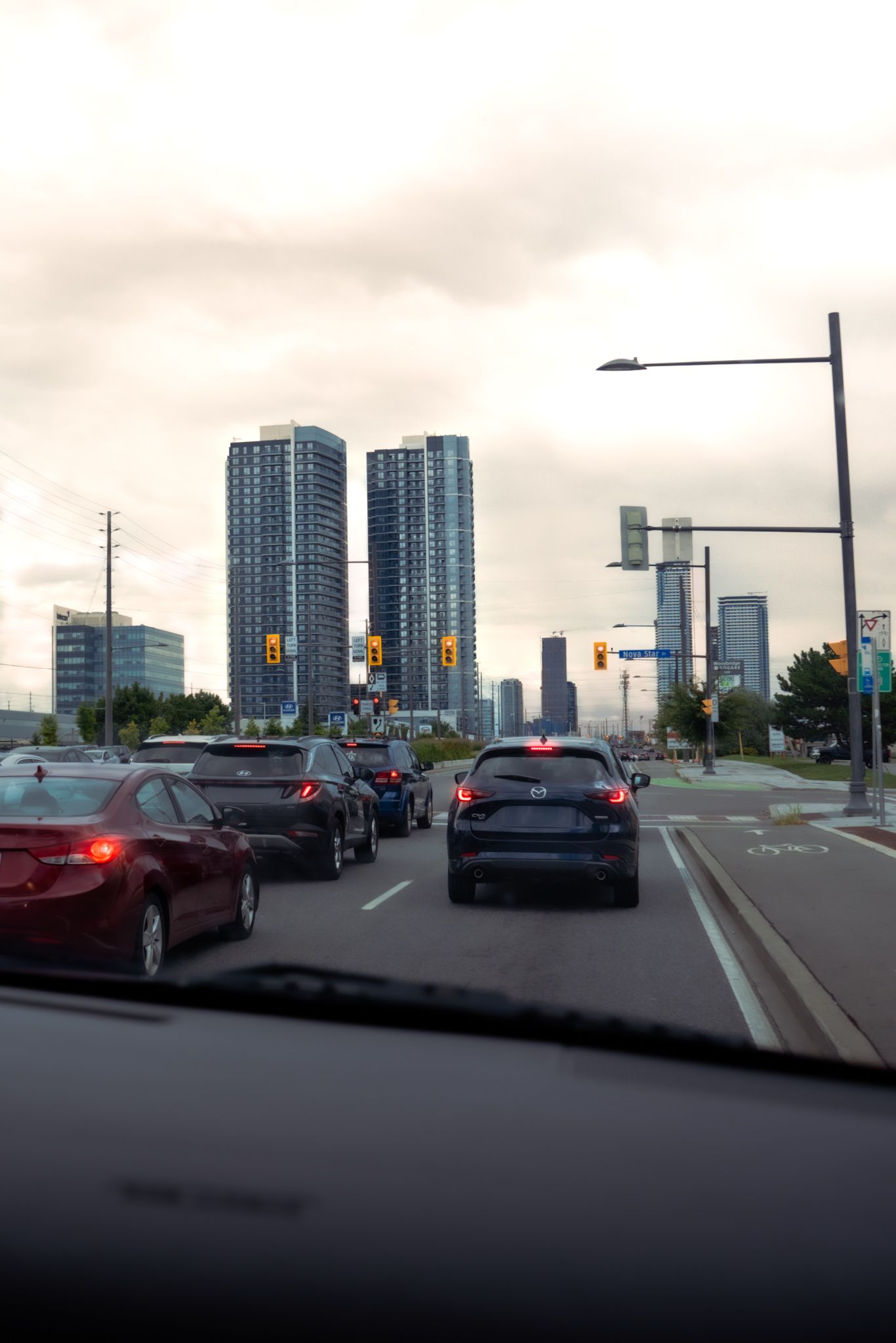 Urban traffic scene with cars waiting at intersection near modern high-rise apartment towers in a city skyline.