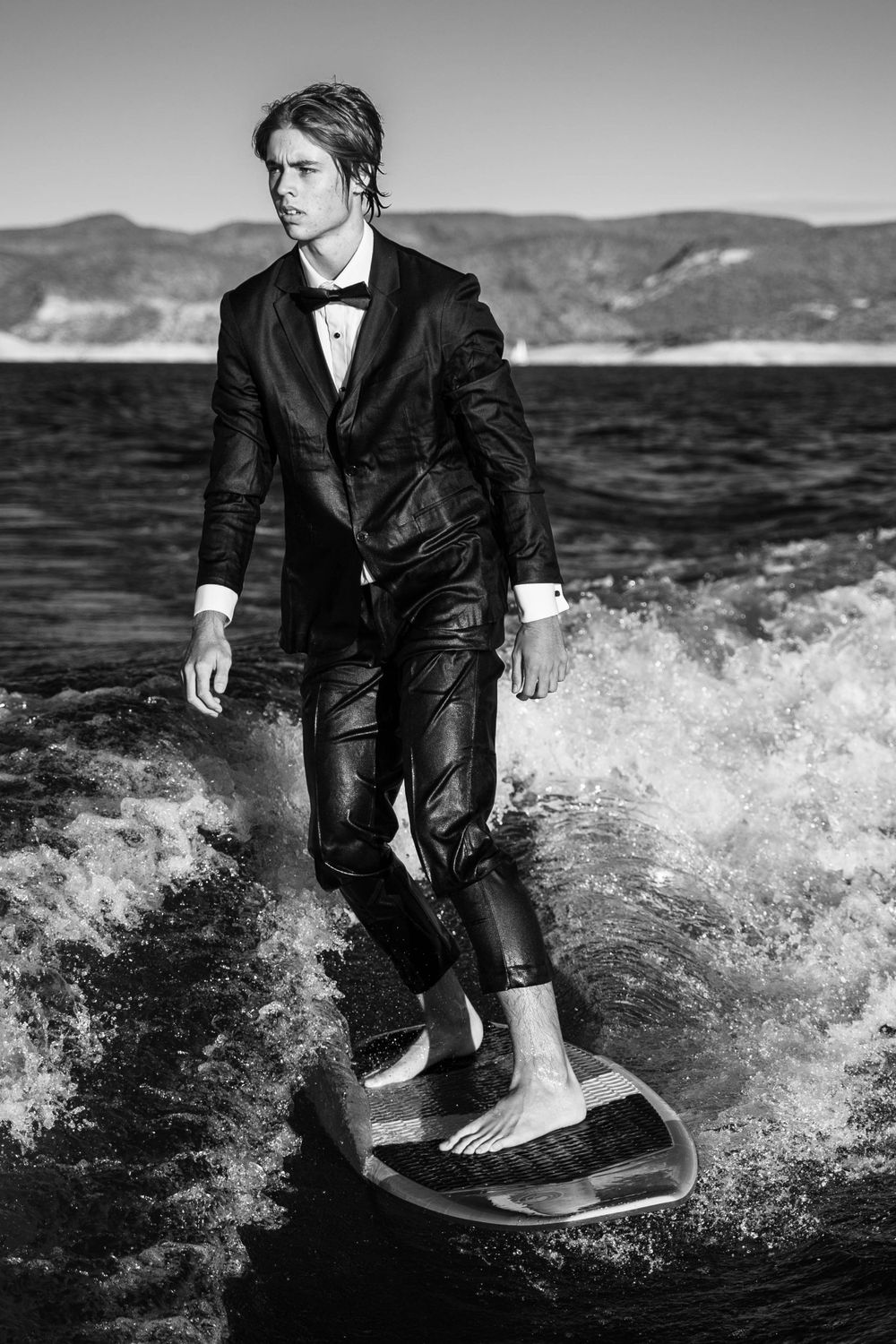 A figure in a wet tuxedo rides waves in a dramatic black and white action shot.