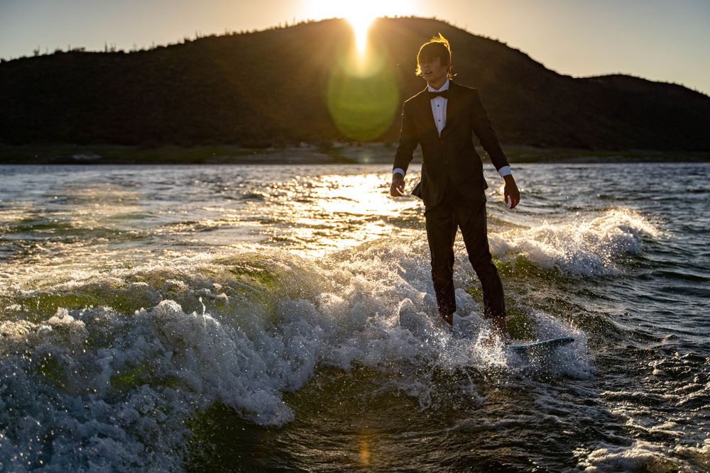 A tuxedo-clad figure rides ocean waves during golden hour with mountains in the background.