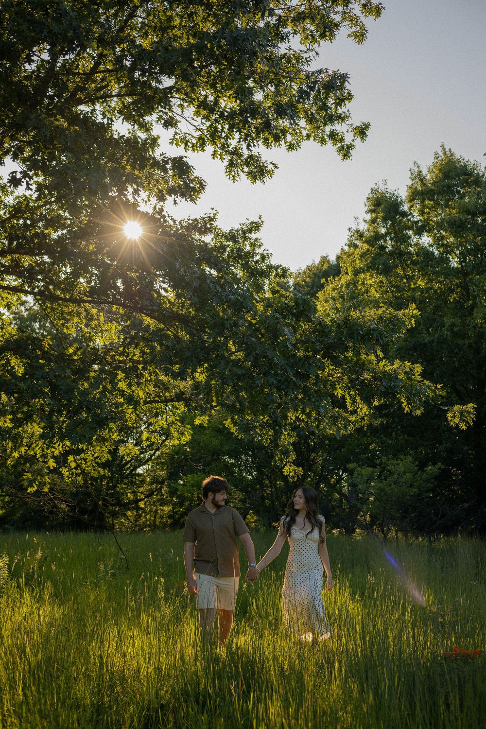 A couple plays and spins in a flower and grass field during their engagement photos in Flushing, Michigan.