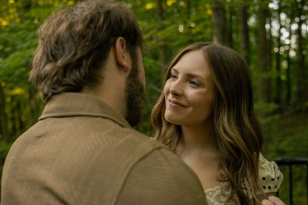 A couple shares an intimate moment while dancing together in a lush green forest setting.