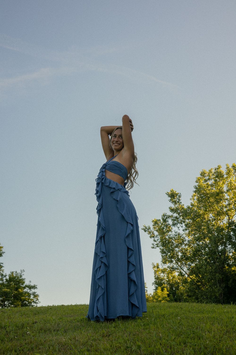 A girl spins and plays around in a long blue boho dress during her senior photos at the Davison Hogbacks in Michigan.